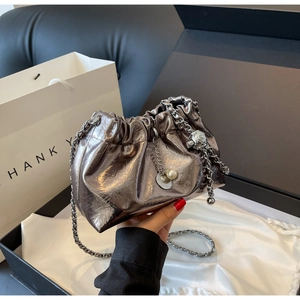 Detail of silver pleated cloud bucket bag with chain strap and pearl charm on white satin