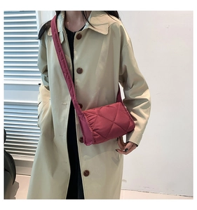 Detail van een magenta gewatteerde crossbodytas gestyled met een beige trenchcoat