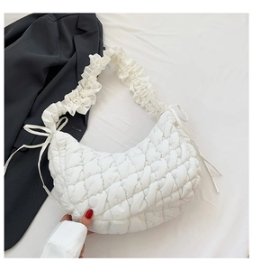 Detail of white quilted dumpling bag with scrunchie strap and bow on dark blazer