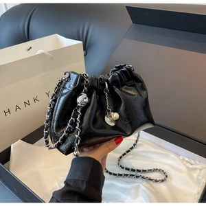 Macro view of black pleated dumpling bag with silver chain and pearl charms in gift box