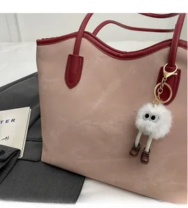 Detail of canvas tote bag with burgundy leather trim and fuzzy monster charm