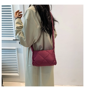 Detail van gewatteerde bordeauxrode crossbodytas met bijpassende stoffen riem op model