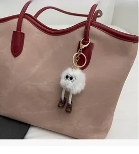Detail of creative plush monster charm with big eyes on a stylish shoulder tote bag