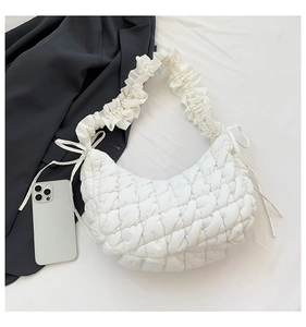 Detailed view of white quilted dumpling bag with ruffled strap and ribbon details
