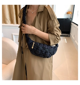 Detail of black quilted cloud bag with gold zipper on a beige trench coat