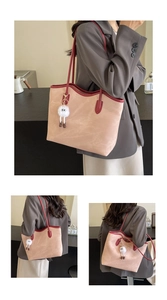 Detail of peach pink leather tote bag with burgundy handles and white plush charm pendant