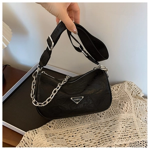 Close-up of black textured leather bag with silver logo and wide woven strap details