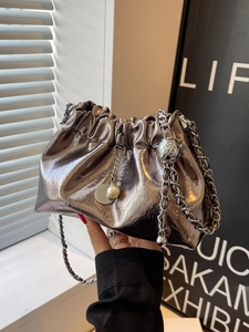 Silver metallic dumpling bag with thick chain strap and pearl charms in a studio setting