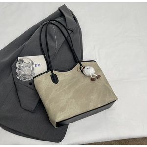 Flat lay of minimalist beige tote bag with black leather trim and plush doll charm