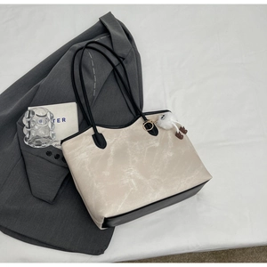 Flat lay of retro marble textured tote bag with black straps and plush monster charm