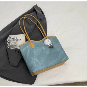 Detail of teal and yellow tote bag with retro leather texture and plush doll charm