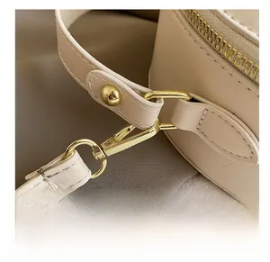 Detailed close-up of golden metal hooks and fine stitching on beige crossbody bag