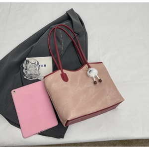 Detail of red and beige patchwork tote bag with plush charm on white cloth