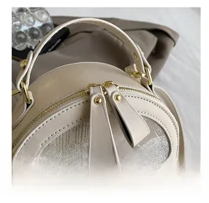 Detailed close-up of the smooth golden metal double zippers on the beige round crossbody bag