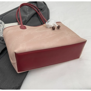 Detail of a large beige tote bag with red leather trim and a white plush toy pendant