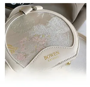 Close-up of floral embroidery on cream circular crossbody bag with gold metal studs