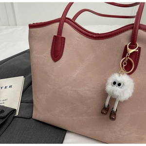 Detail of color-block tote bag with plush monster charm on a minimalist background