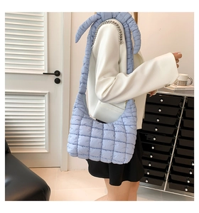 Detail of light blue quilted puffer bag with chic chain and fabric strap on a model