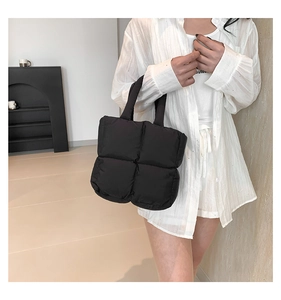 Side view of a black quilted down tote bag worn by a model in a minimalist setting