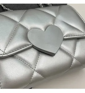 Close-up of silver quilted crossbody bag with heart-shaped buckle and metal chain strap