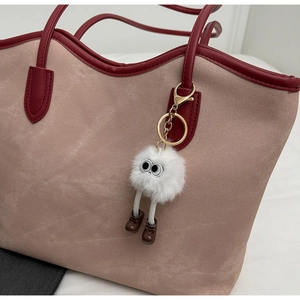 Close-up of white plush monster charm with big eyes and leather shoes on a tote bag
