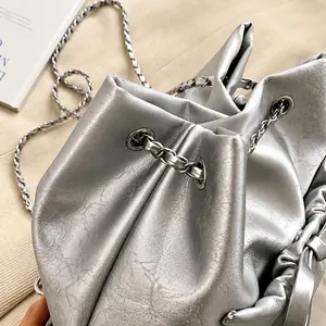 Detalle del bolso tipo saco plateado con cordón, cadena metálica y correa de cuero