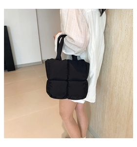Close-up of black quilted puffer tote bag with padded handles shown on model