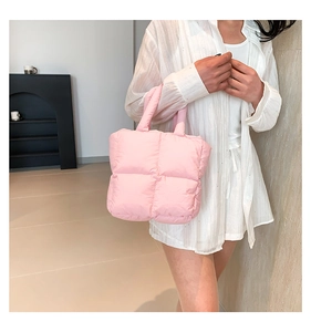 Detail of pink puffy tote bag showing quilted texture and soft padded handles on model