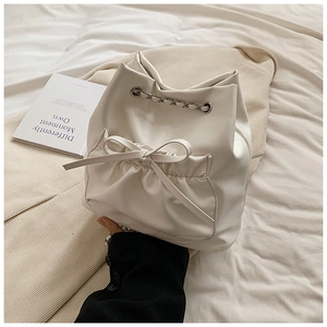 Detalle del bolso tipo cubo blanco con bolsillo de lazo y correa de cadena metálica