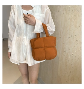 Detail of orange puffer tote bag featuring quilted nylon fabric and padded top handles
