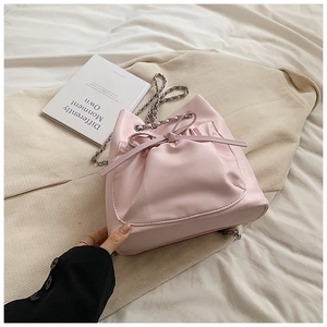 Primer plano de bolso saco rosa con cadena y cordón de lazo sobre tela blanca