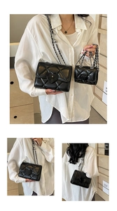 Close-up of black quilted shoulder bag with heart lock and mini pouch charm on chain strap