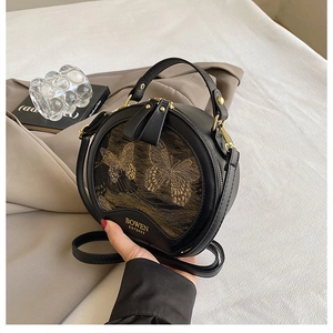 Detail of round black handbag with gold butterfly motif and textured leather finish