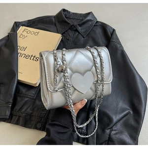 Close-up of silver quilted crossbody bag with heart ornament and chain strap