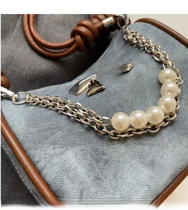 Close-up of elegant silver metal chain and white faux pearl strap on a grey bag