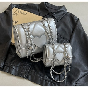 Detail of silver quilted chain bags with heart charms on a black leather background