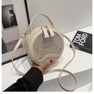 Detail of round off-white crossbody bag featuring pink floral embroidery and gold hardware