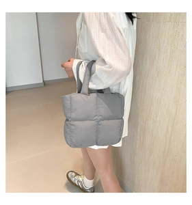 Close-up of a grey quilted puffer tote bag with glossy nylon texture on a model