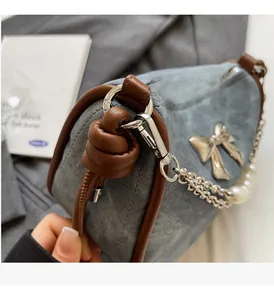 Detail of blue denim shoulder bag with brown leather trim and silver bow metal hardware