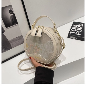 Detail view of round crossbody bag with floral embroidery and golden metal hardware