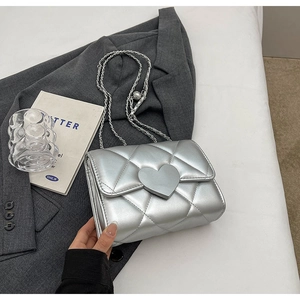 Detail view of silver quilted crossbody bag with heart lock on grey blazer fabric