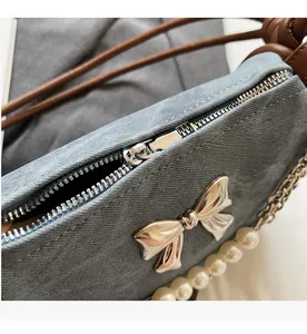 Detail of denim bag featuring smooth zipper, metal bow charm, and pearl chain strap