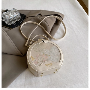 Detail of round cream handbag featuring floral patterns and gold anti-wear bottom studs