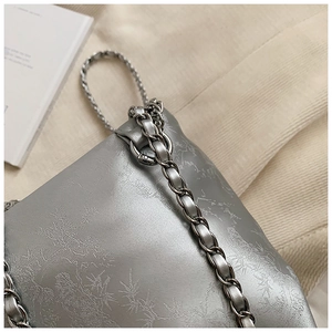 Detalle del bolso de cubo en jacquard gris plata con cadena de metal y tira de cuero