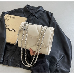 Macro detail of beige quilted leather bag with heart ornament and adjustable chain strap