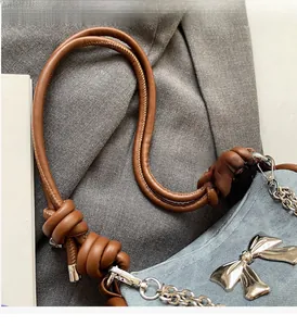 Detail of blue denim shoulder bag featuring silver metal bow and sturdy leather handle