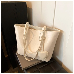 Detail of cream tote bag with pleated leather texture and heart shaped charm accessory