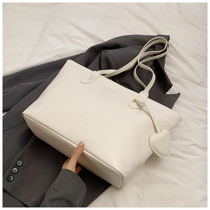 Macro detail of white leather tote bag texture featuring a heart-shaped charm and strap