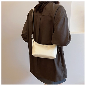 Detail of off-white dumpling bag with diamond quilted pattern worn on shoulder