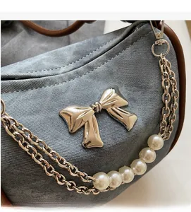 Close-up of grey denim handbag with silver metal bow and decorative pearl chain